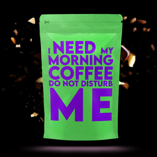 Felgroene koffiezak met paarse tekst waarop staat: "I need my morning coffee. Do not disturb me", tegen een donkere achtergrond met zwevende koffiestukjes.